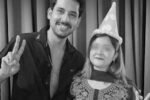 "A man and a woman wearing a birthday party hat smiling and showing peace signs in a black and white photo"