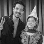 "A man and a woman wearing a birthday party hat smiling and showing peace signs in a black and white photo"